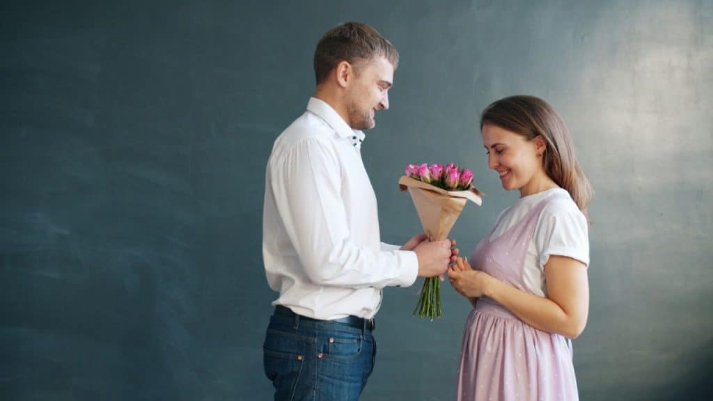 Smiling man in a white shirt giving a bouquet of pink roses to a woman.