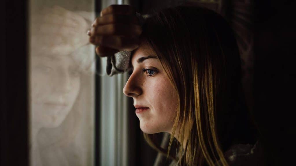 A woman leaning against a window and looking outside thoughtfully.