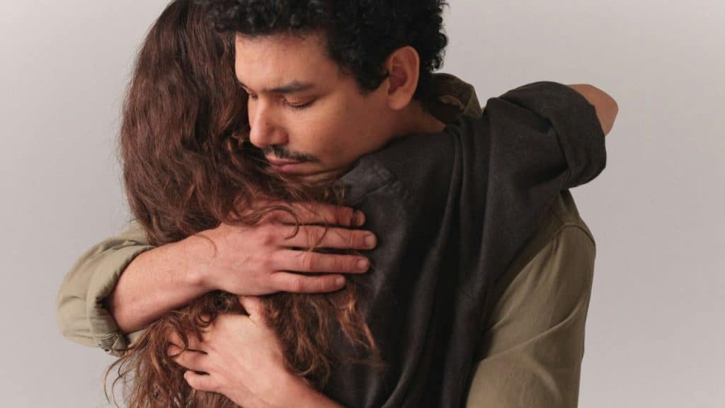 Man with a mustache hugging a woman with long, brown, wavy hair.