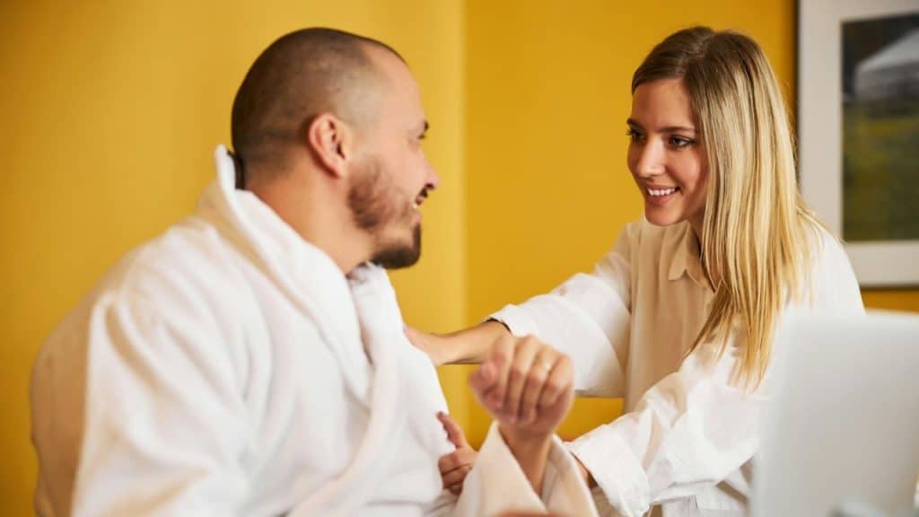 Balding man in a white robe smiles at a blonde woman in a white shirt.