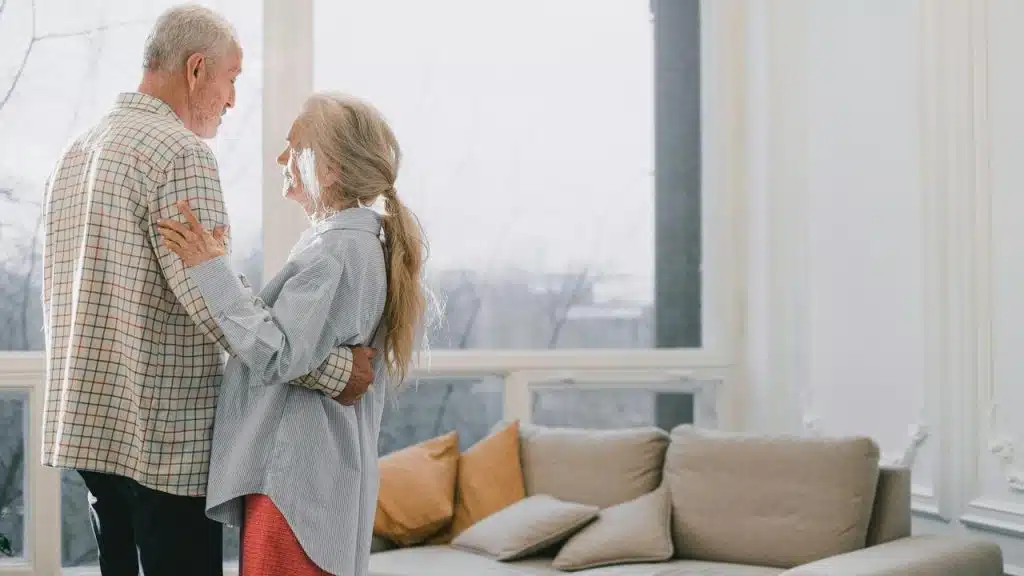 A senior couple dancing together in a bright living room.