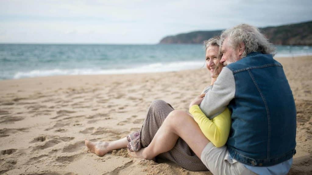 A senior couple sitting together and embracing on a beach.