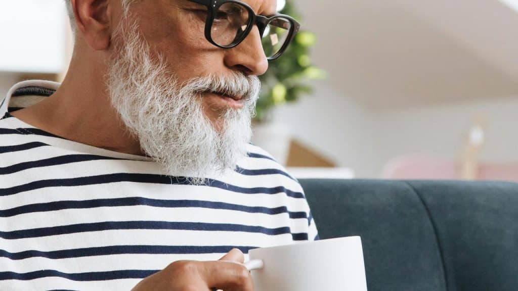 A senior man holding a white mug while sitting.