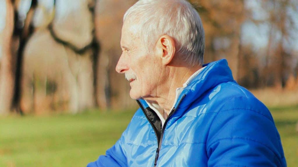 A senior man in a blue jacket sitting outdoors.