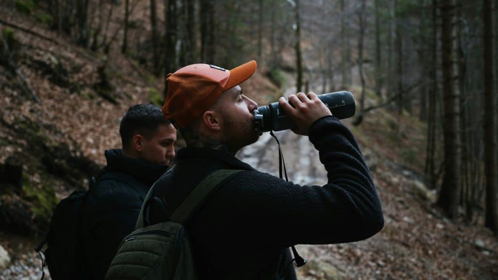 A man trekking with his friend and drinking water from a bottle.