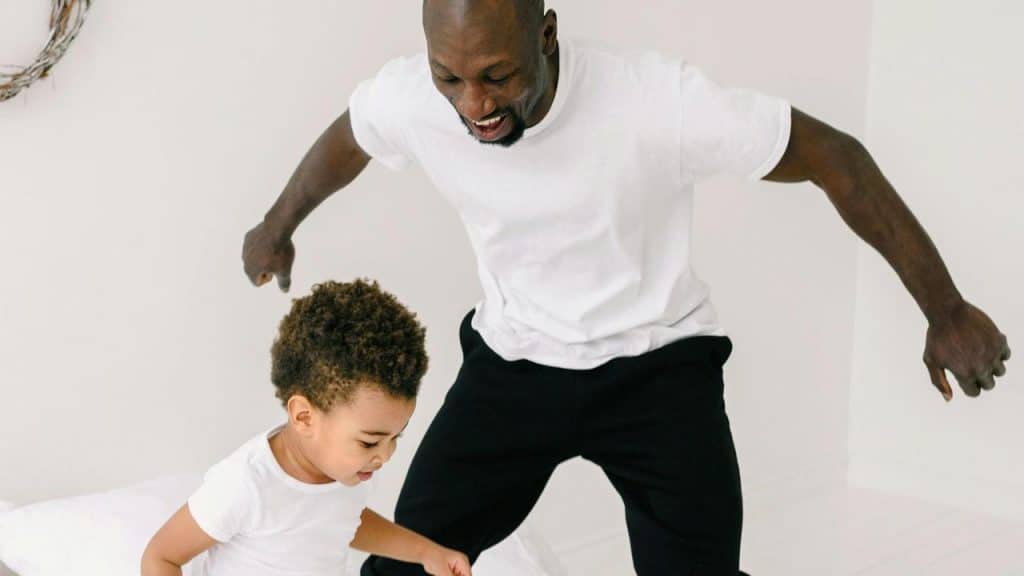 A father playing and jumping on the bed with his child.