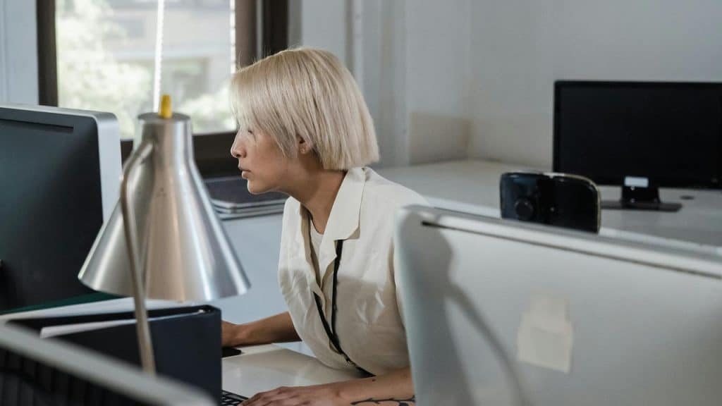 A woman with short blonde hair working at a computer in an office.