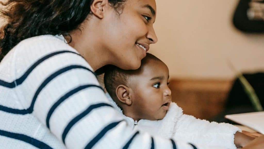 A smiling mother holding her baby close while sitting together indoors.