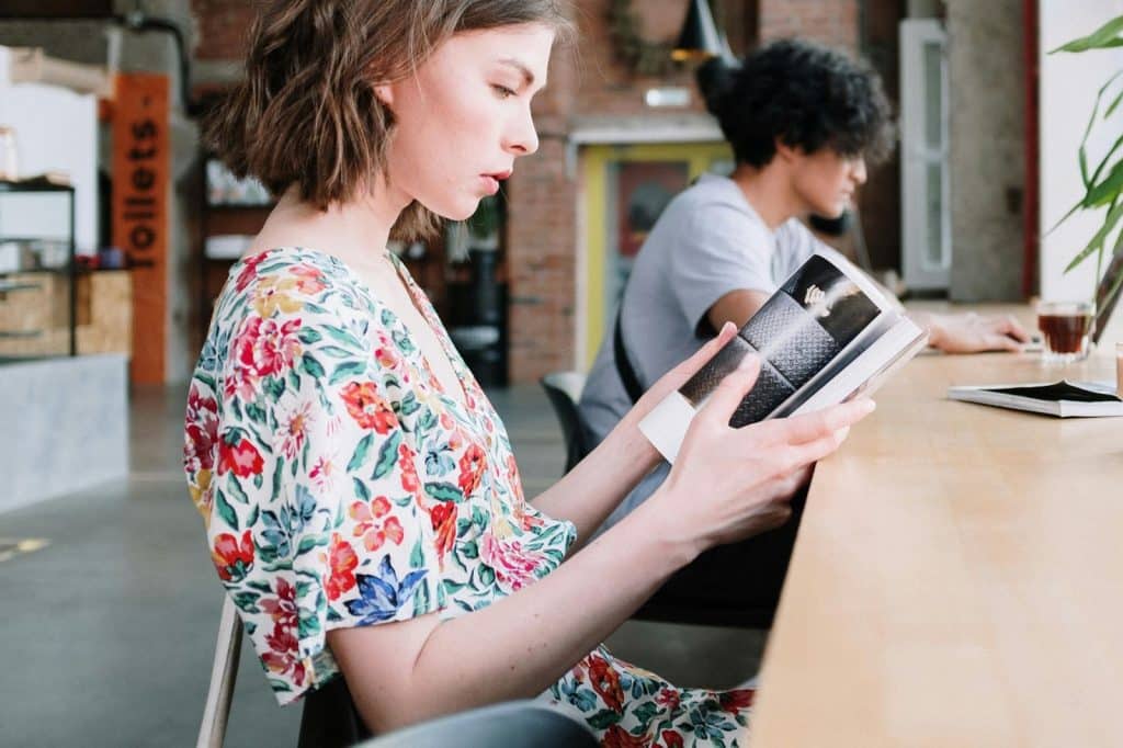 A woman reading a book and a man using a laptop 