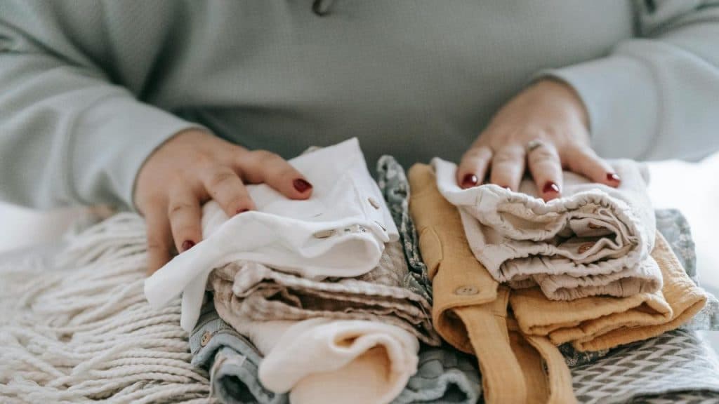 A person folding neatly stacked baby clothes on a table.
