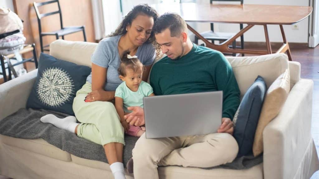 A family sitting on a couch looking at a laptop together.