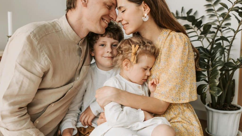 A happy family sitting together with parents embracing their two young children.