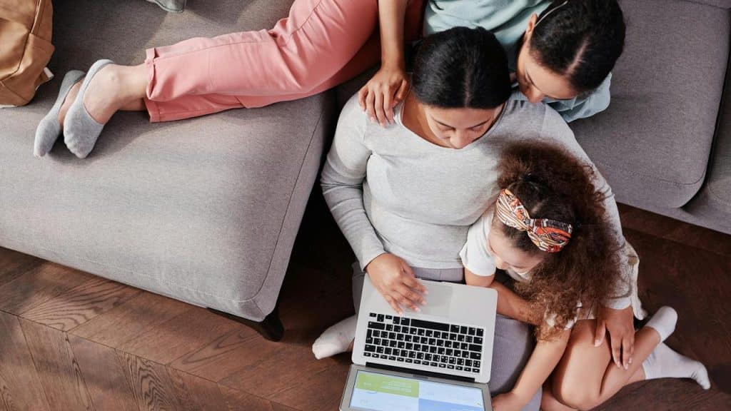 A woman using a laptop on the floor with her children beside her.