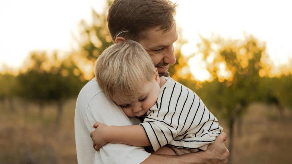 A father hugging his young child outdoors at sunset.