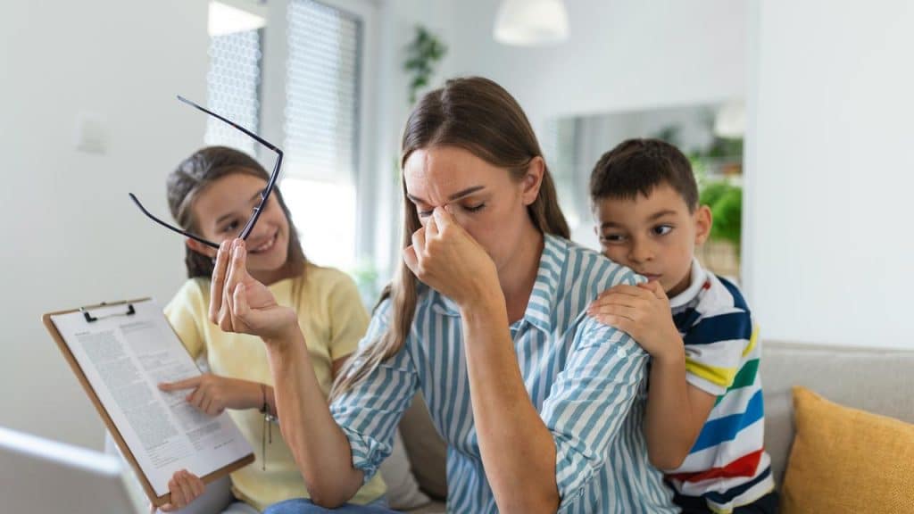 A stressed mother sitting on a couch with two children beside her.