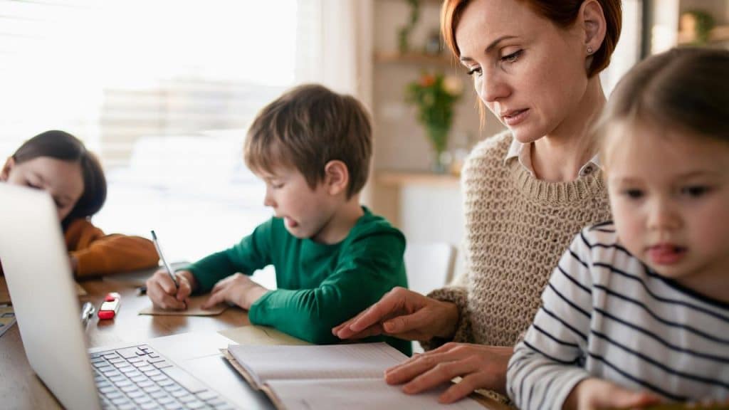 A mother helping her children with homework at a table.