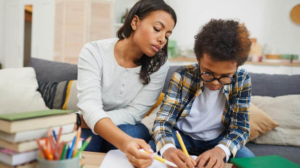 A mother helping her son with homework at a table.