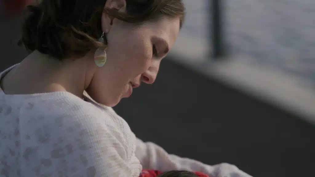 A mother cradling her baby while sitting near the water.
