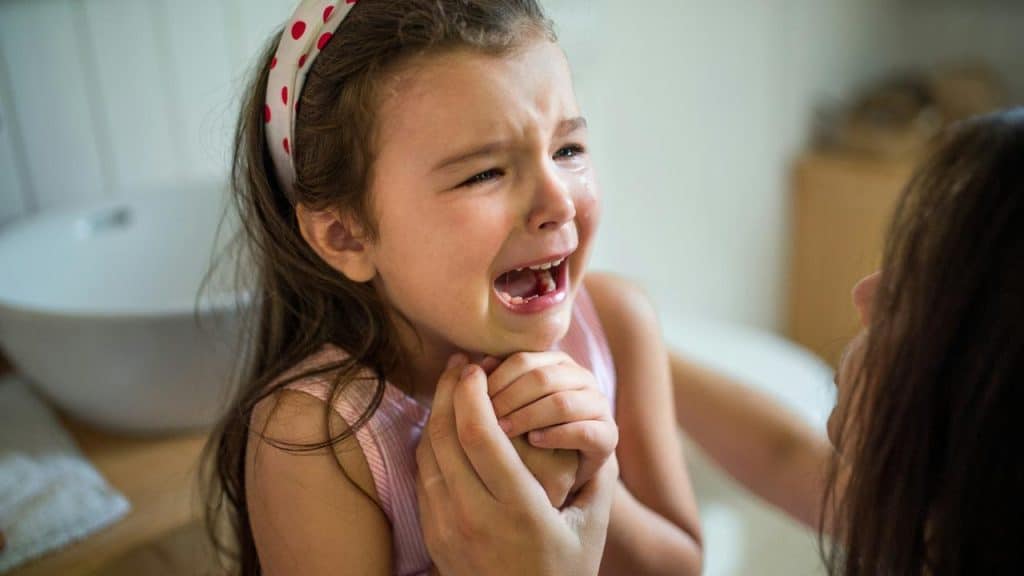 A young girl crying while someone holds her hands.