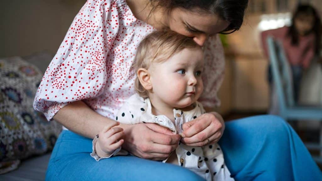 A mother sitting with her toddler on her lap, gently kissing their head.