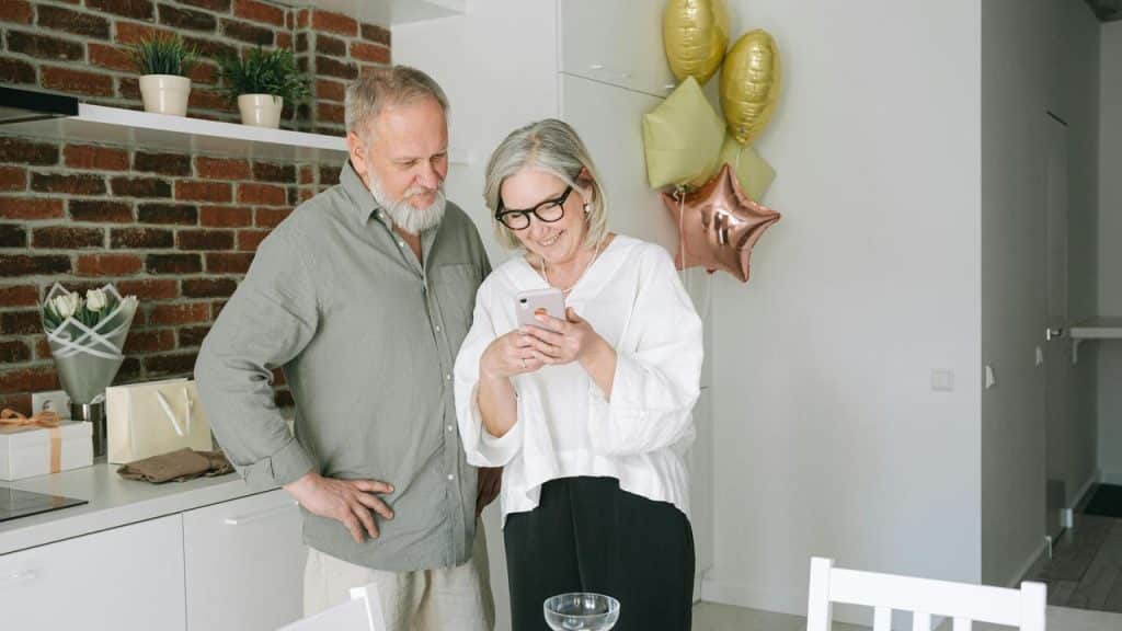 A couple smiling while looking at a phone together in the kitchen.