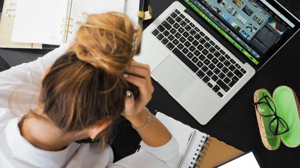 A woman sitting at a desk with her head in her hands in front of a laptop.