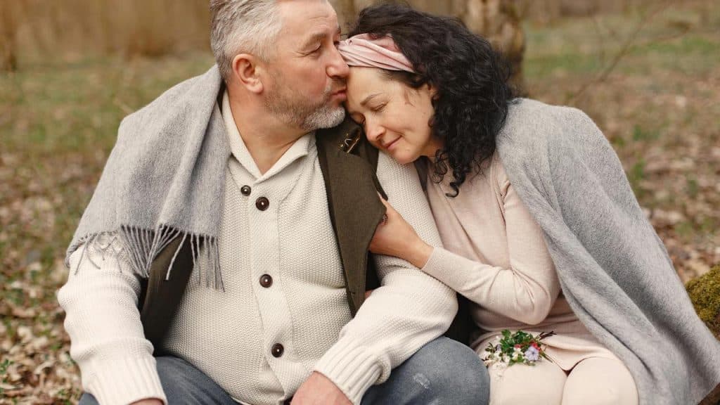 A man kissing a woman’s forehead as they sit close together outdoors.