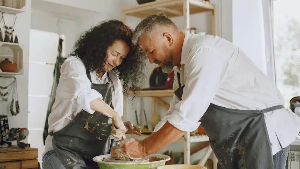 A couple shaping clay together on a pottery wheel.