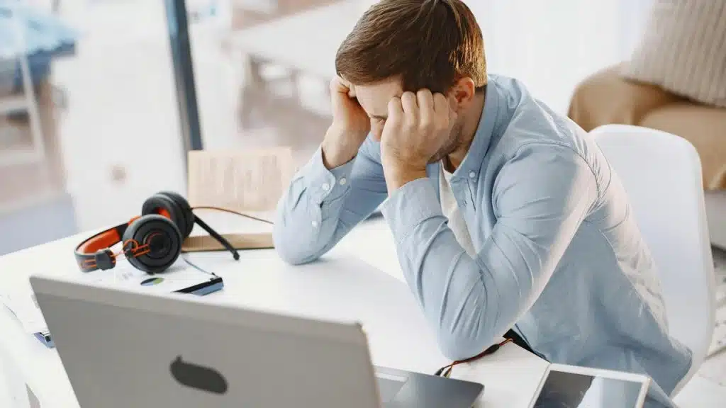 A man sitting at a desk with his head in his hands in front of a laptop.