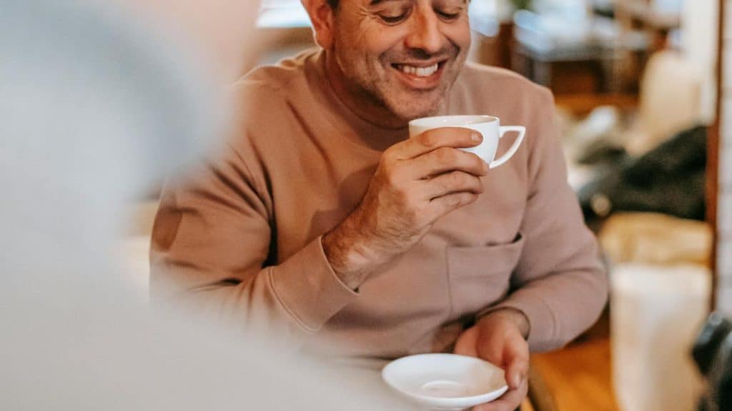 A man smiling while holding a cup of coffee.