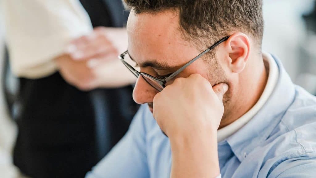 A man wearing glasses resting his chin on his hand looking down.