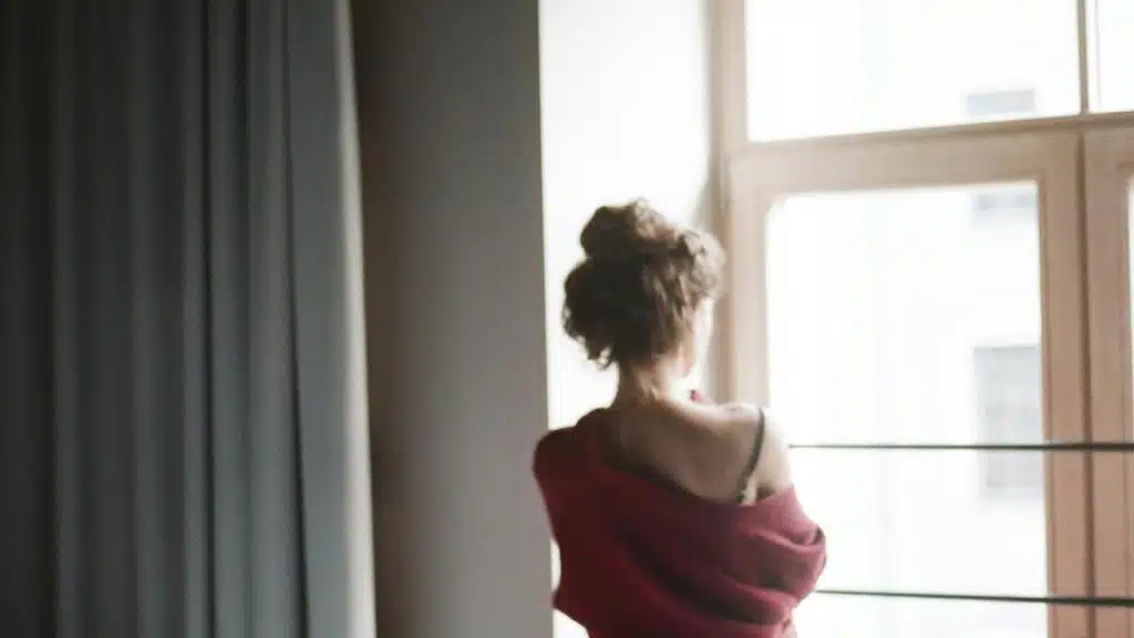 A woman standing by a window with her back to the camera.