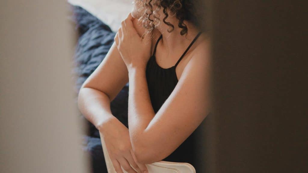 A woman sitting on a chair with her hand resting on her shoulder.