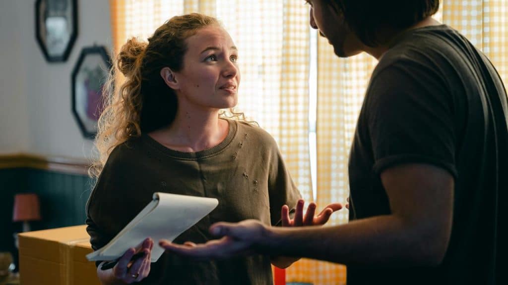 A woman holding a notepad talking to a man indoors.
