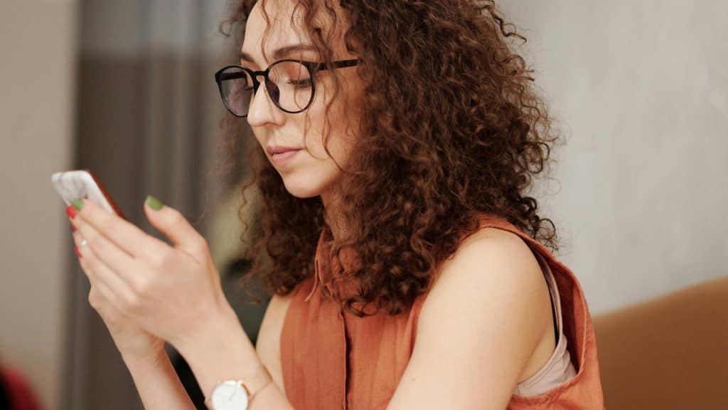 A woman with curly hair and glasses looking at her phone.