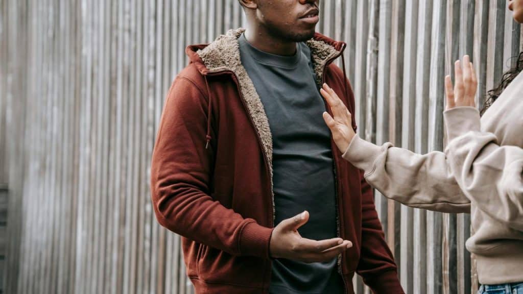 A man talking to a woman who is holding up her hand in refusal.