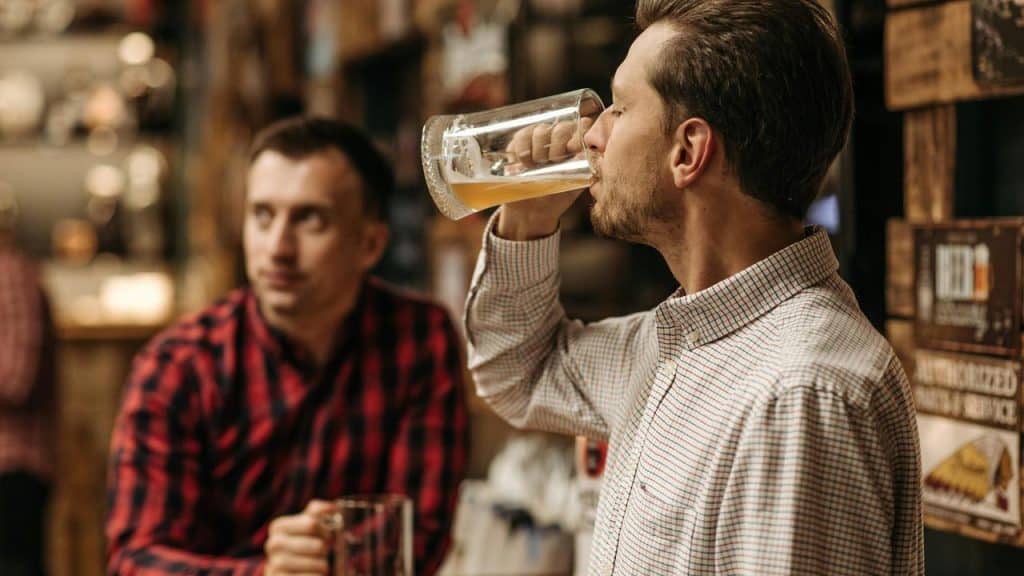 A man drinking beer at a bar with a friend nearby.