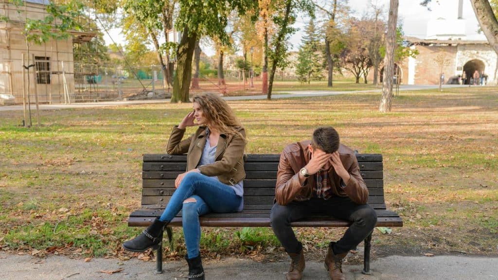 A couple sitting on a park bench looking upset.