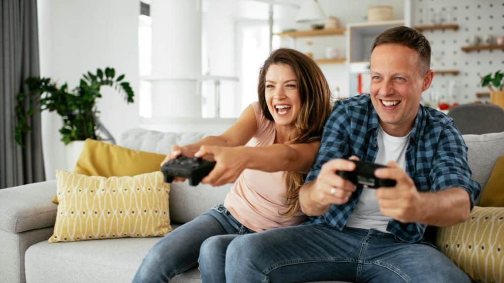 A couple laughing while playing video games on the couch.