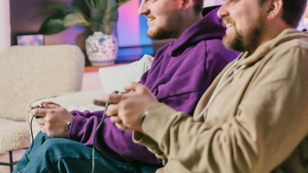 A pair of friends smiling while playing video games on the couch.