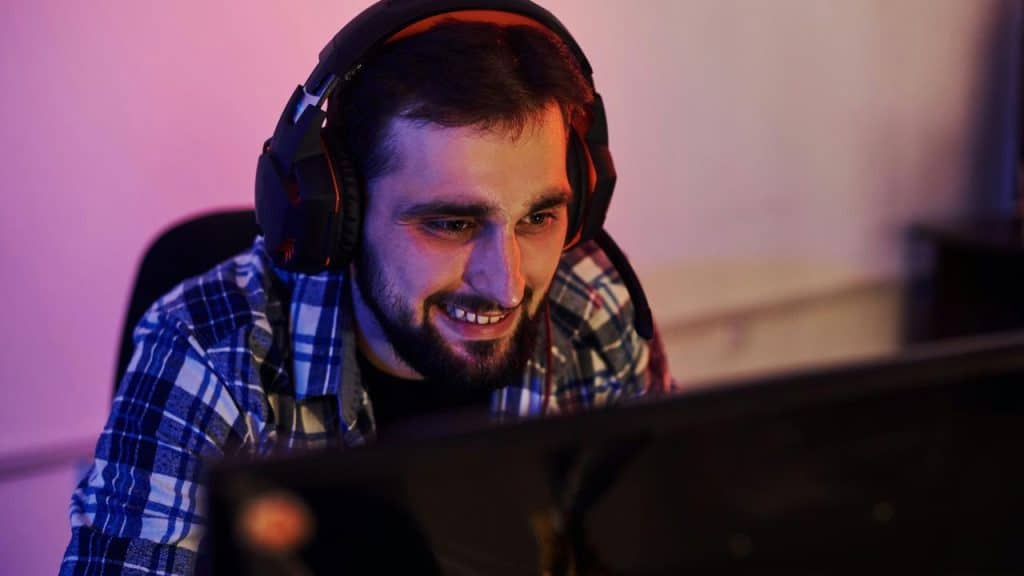 A man smiling while playing video games on a computer with headphones on.