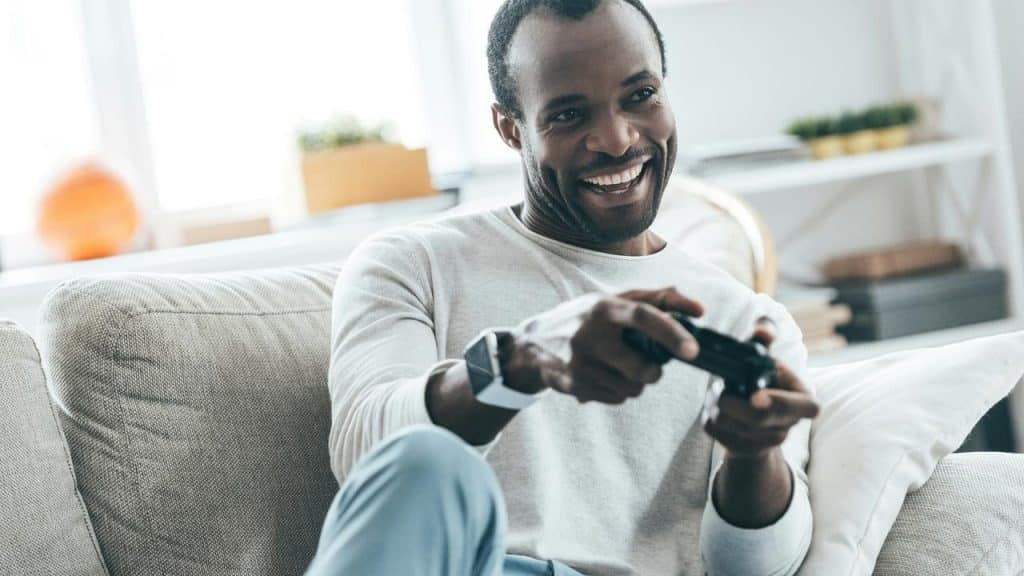 A man smiling while playing video games on the couch.