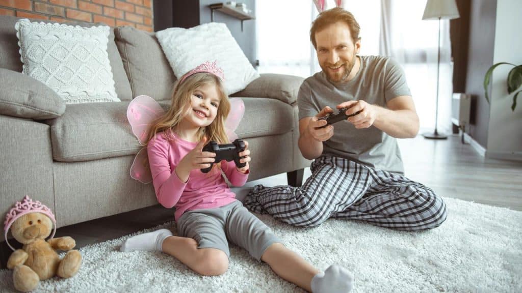 A father and daughter smiling while playing video games on the floor.