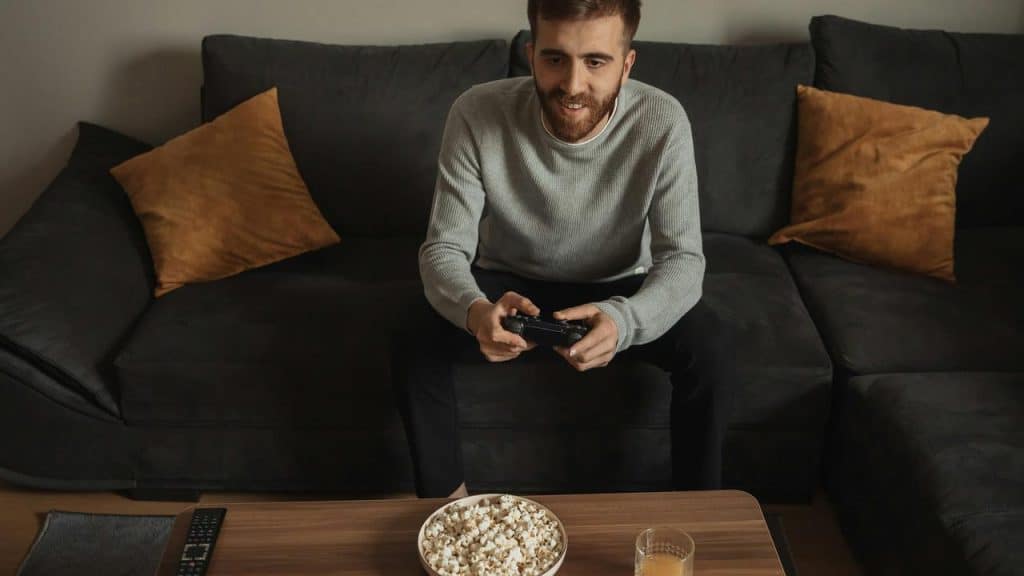 A man playing video games on the couch with popcorn and juice on the table.