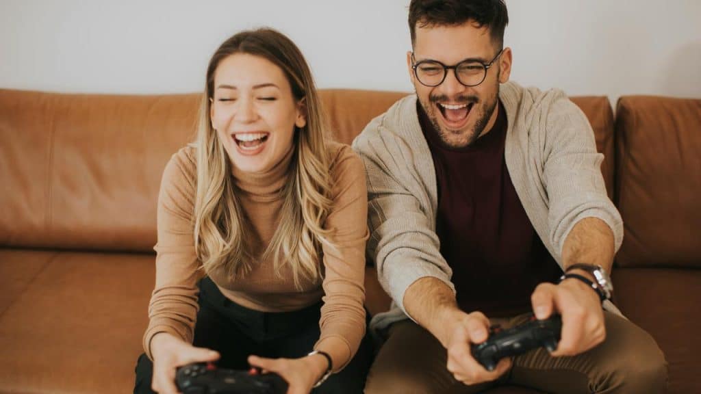 A woman and a man smiling while playing video games on the couch.