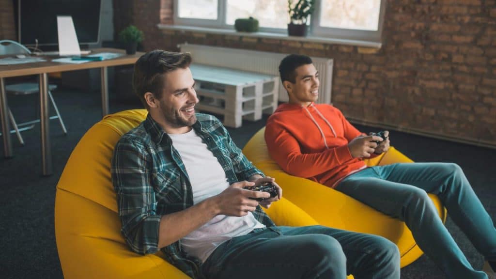 A pair of friends playing video games on yellow beanbags.