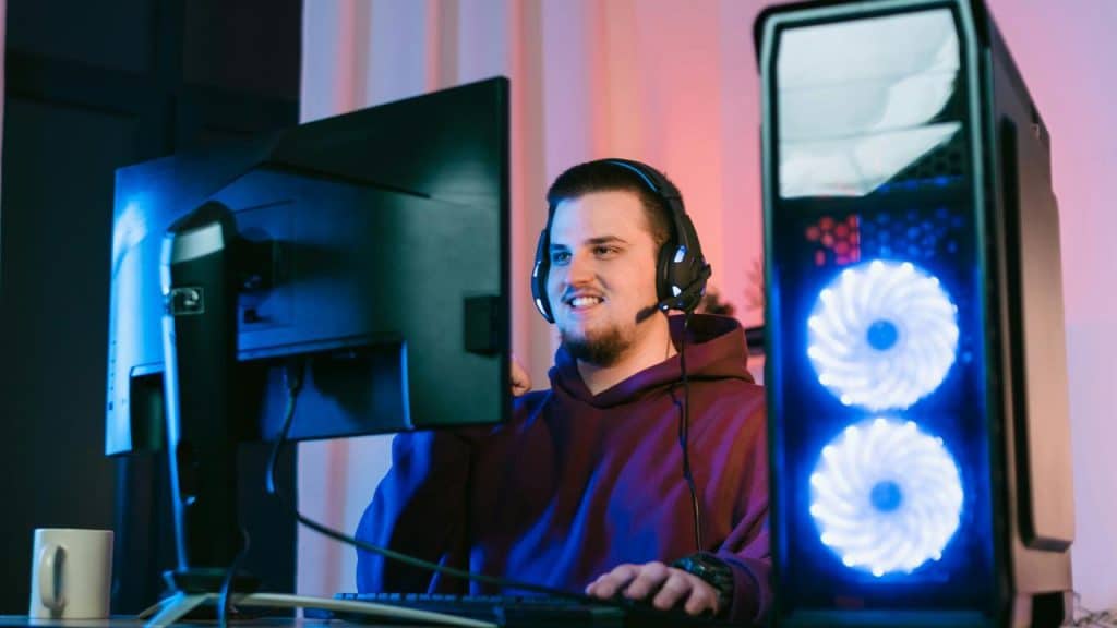 A man smiling while playing video games on a computer with a headset on.