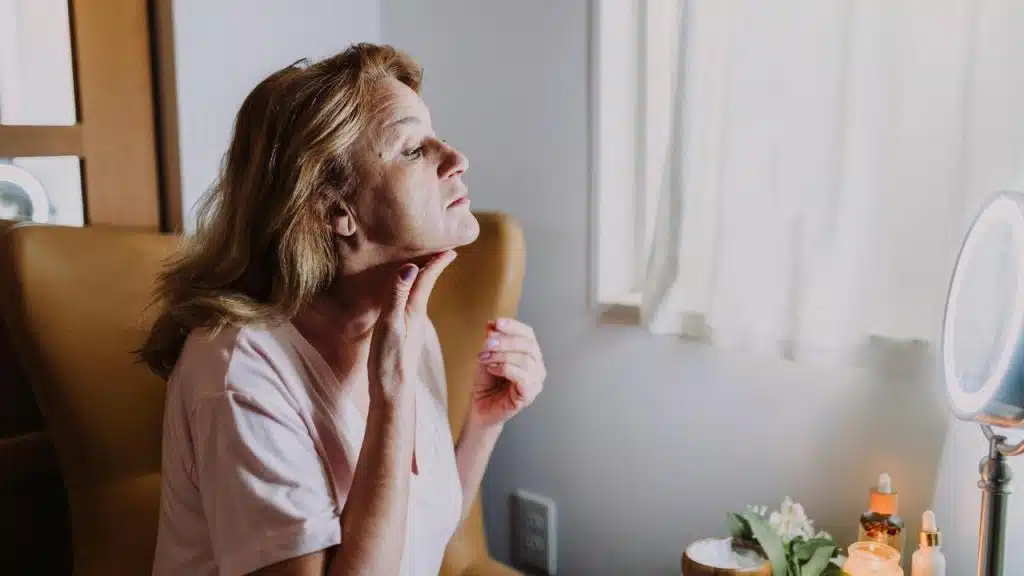 A woman examining her neck in a mirror.