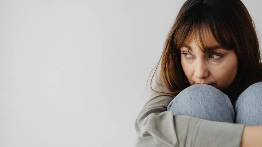 A woman sitting with her knees pulled to her chest looking to the side.