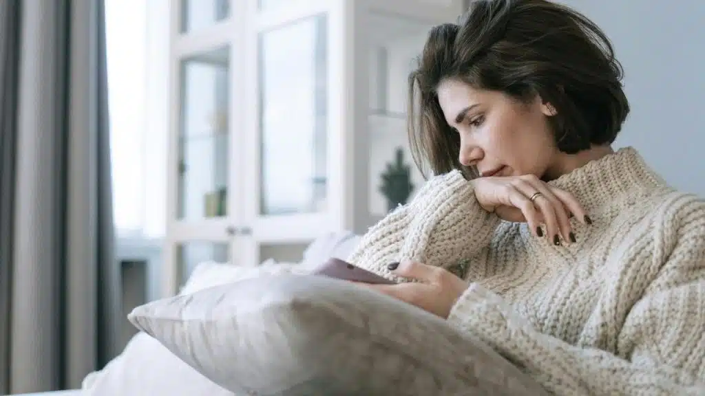 A woman sitting on a couch looking at her phone thoughtfully.